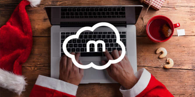 mCloud logo preko slike ruku Deda Mraza koje kucaju na lap topu a pored je njegova crvena kapica